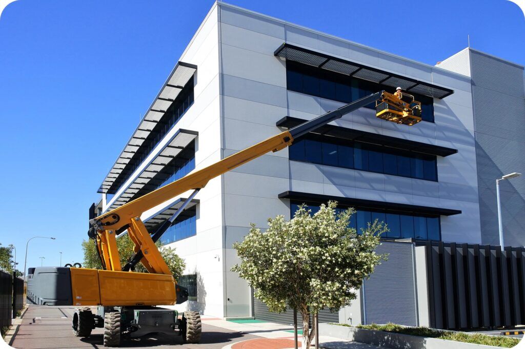 Worker operating boom lift for overhead installation at a construction site under blue sky.