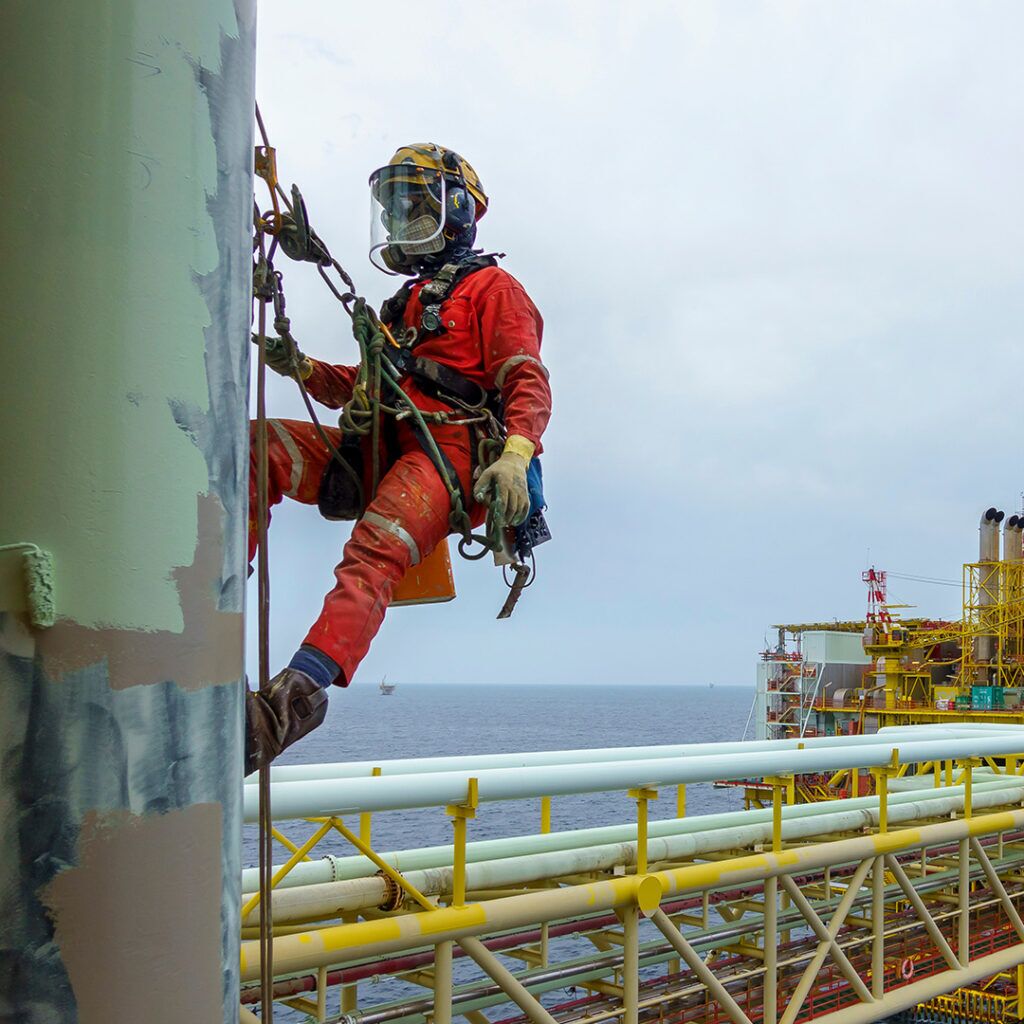 A worker on a oil rig in ocean using safety harness while working at heights