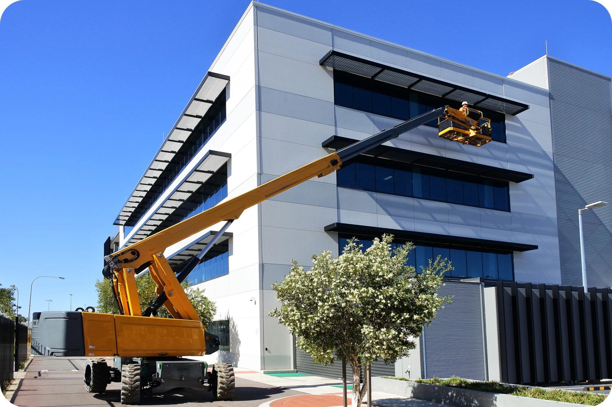 Worker operating boom lift for overhead installation at a construction site under blue sky.