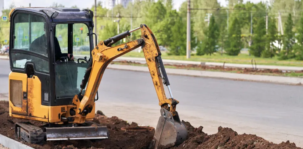 Mini excavator trenching near a roadway with focus on visibility, stability, and operator safety training